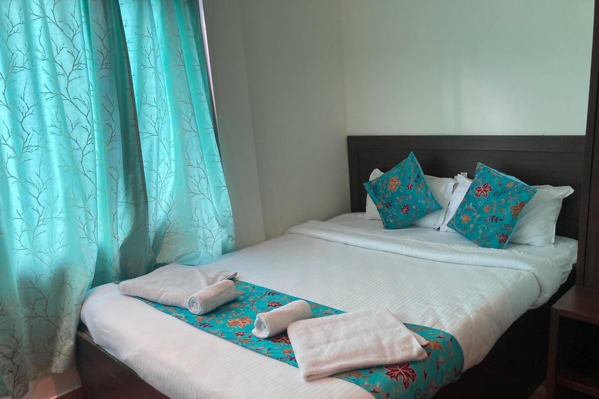 A neatly made bed with white linens, two decorative pillows, and a rolled towel on a patterned bedspread.