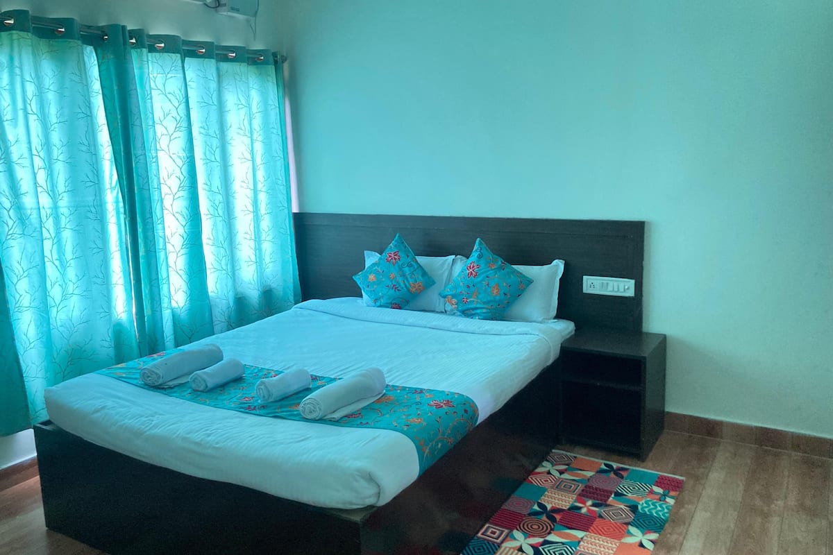 A neatly made bed with white linens and blue patterned pillows, a dark wooden headboard, and a patterned rug on a wooden floor.