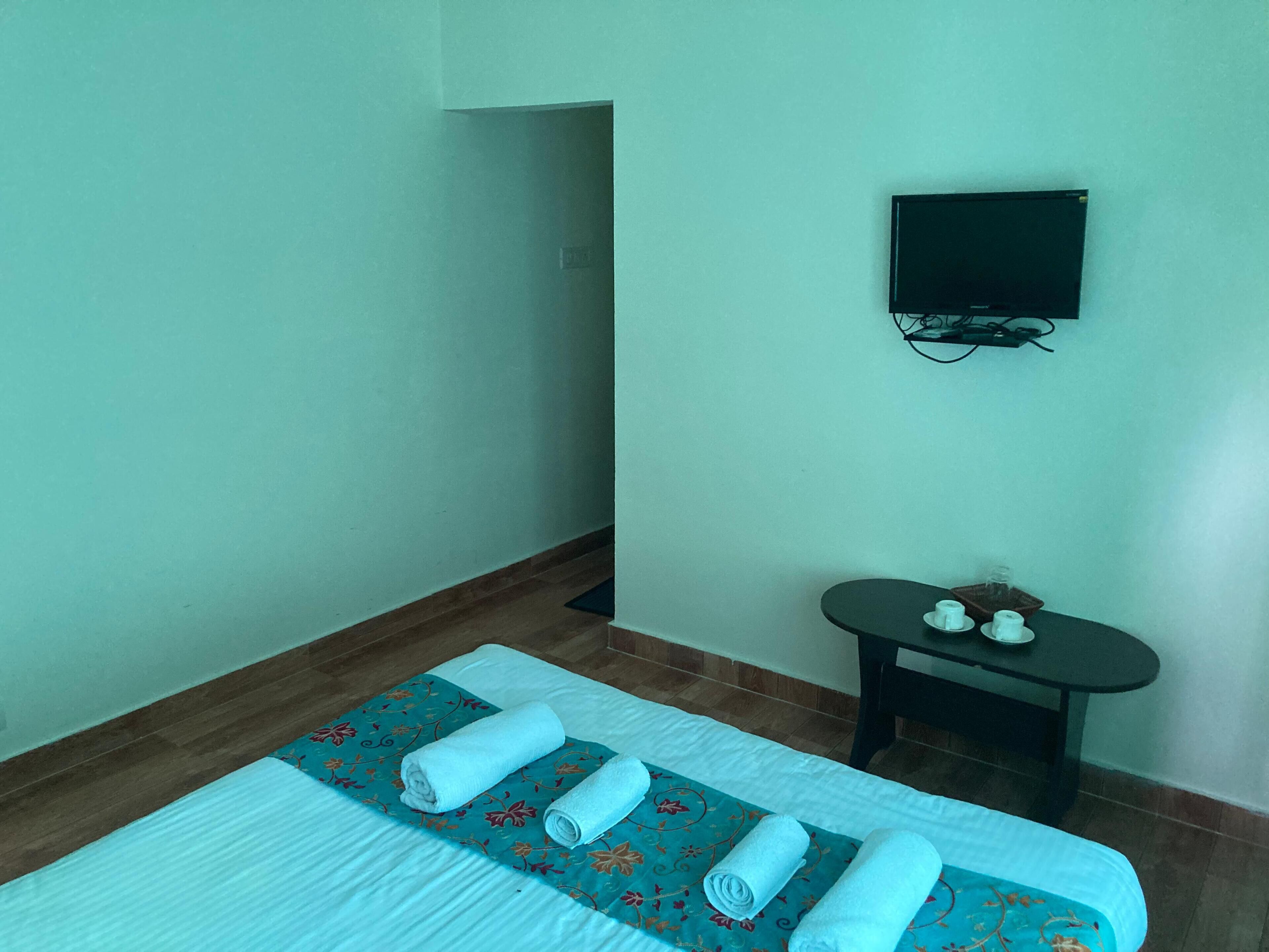 Habitación de hotel con una cama, una mesita con un vaso y un televisor de pantalla plana montado en la pared.