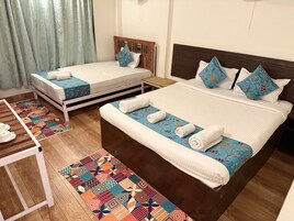 A hotel room with two beds, a wooden nightstand, a patterned rug, and a small table with cups and a plate.