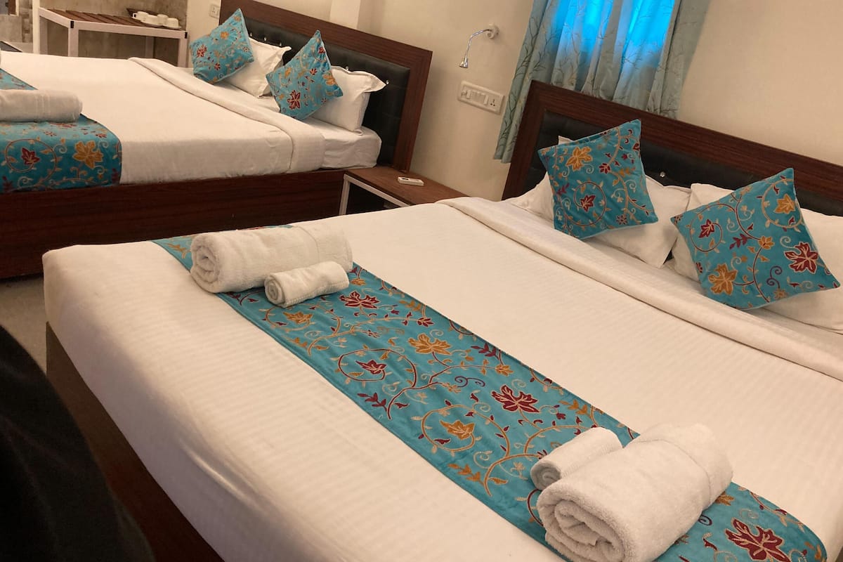 A hotel room with two beds, each with a blue floral bedspread and white linens. There are two white towels on each bed.