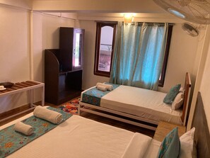 A hotel room with two beds, a TV, a small table with a tray, and a window with curtains. - Rest Nest - Havelock (Port Blair)