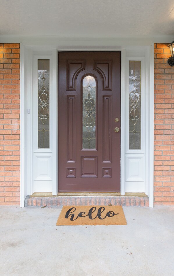 A brown front door with a glass panel and a doormat with "hello" written on it.