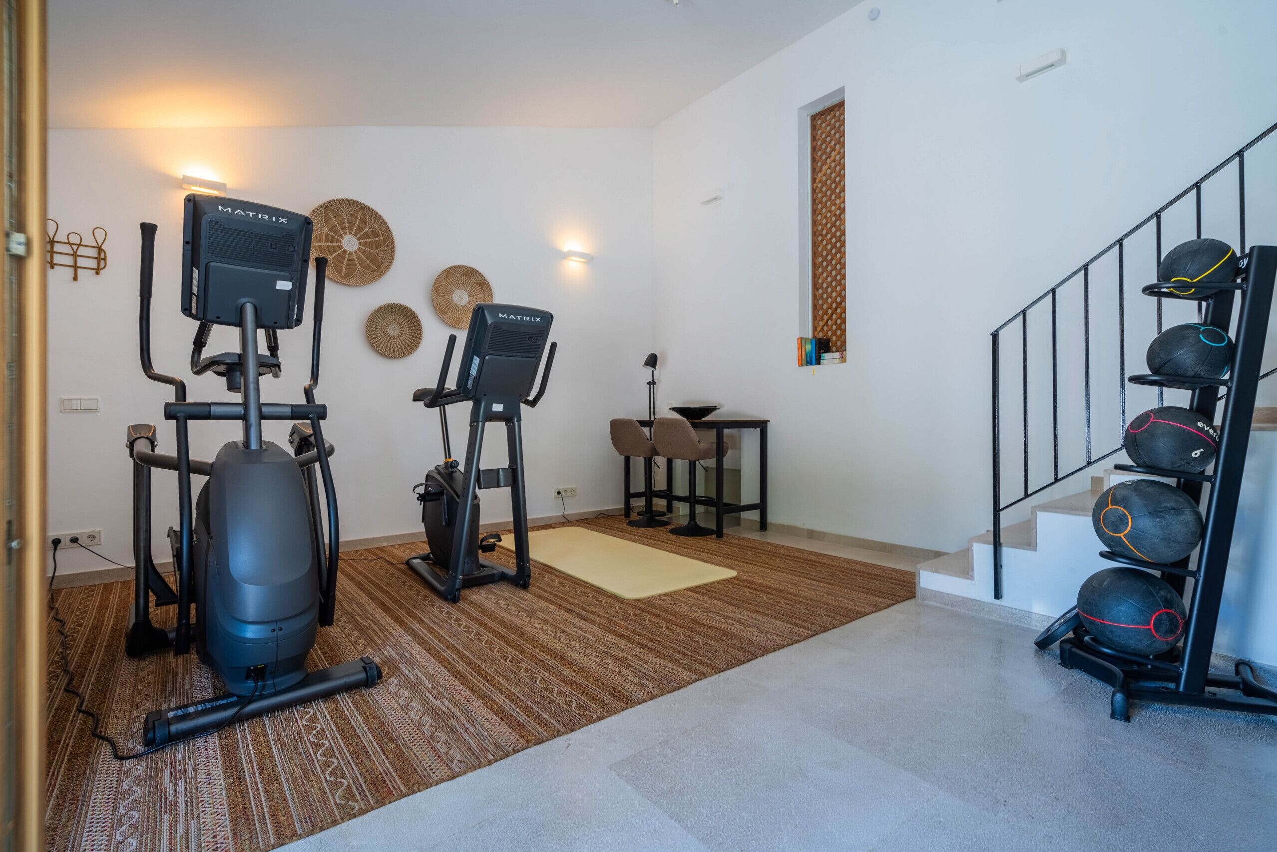 Une salle de sport à domicile équipée de deux vélos d’appartement, d’un tapis de course et d’un porte-balles d’exercice.