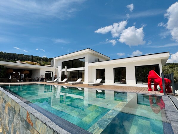 A modern house with a swimming pool, lounge chairs, and a red sculpture.
