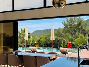A modern poolside area with lounge chairs, a dining table, and umbrellas.