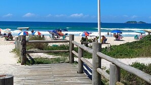 A wooden boardwalk leading to a beach with umbrellas and people.