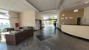 A spacious lobby with a reception desk, a seating area with wicker furniture, and a large window offering a view of the outside.