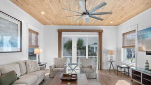 A spacious living room with a wooden ceiling, a ceiling fan, a large window with blinds, a sofa, two armchairs, a coffee table, and a TV on a stand. - Luxury Beach House Steps to Beach (Destin)
