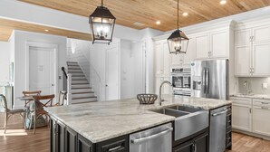 A modern kitchen with a large island, stainless steel appliances, and wooden flooring. - Luxury Beach House Steps to Beach (Destin)