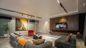 A modern living room with a grey sectional sofa, a red armchair, and a flat-screen TV mounted on a wooden wall. - Zimmys Apartment (Abuja)