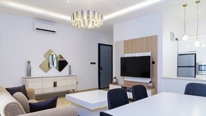 A modern living room with a white sofa, a dining table, and a TV. - Zimmys Apartment (Abuja)