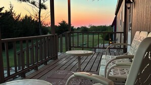 A wooden deck with outdoor furniture, a view of the sunset, and a grassy area in the background. - Spacious 3BR Rural Home + Barn Theater One Hour from Dallas, Fort Worth & Waco (Rice)