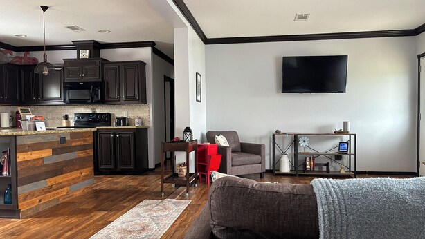 A modern kitchen with dark cabinetry and a wooden island, a living area with a gray sofa and a red chair, and a flat-screen TV mounted on the wall. - Spacious 3BR Rural Home + Barn Theater One Hour from Dallas, Fort Worth & Waco (Rice)