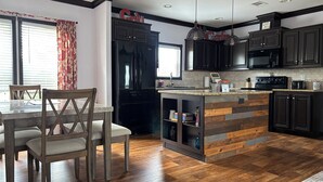 A modern kitchen with dark cabinetry, a wooden island, and a dining area with a table and chairs. - Spacious 3BR Rural Home + Barn Theater One Hour from Dallas, Fort Worth & Waco (Rice)