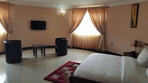 A hotel room with a bed, two chairs, a small table, a TV, and a window with curtains. - Top-Notch Suites and Apartment (Abuja)