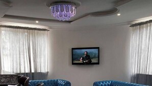 A modern living room with two blue leather sofas, a chandelier, and a framed picture on the wall. - Top-Notch Suites and Apartment (Abuja)