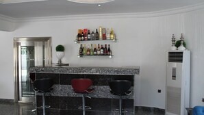 A bar area with a marble countertop, three black bar stools, and a wine shelf above. - Top-Notch Suites and Apartment (Abuja)