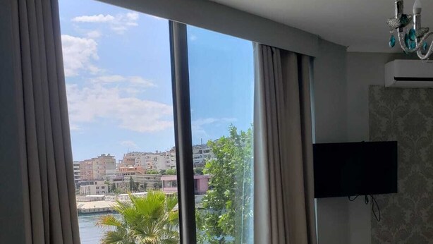 A hotel room with a large window, a bed with neatly folded towels, and a flat-screen TV mounted on the wall.