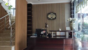 A reception desk with a clock, a desk lamp, and a vase with flowers.