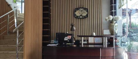 A reception desk with a clock, a desk lamp, and a vase with flowers.