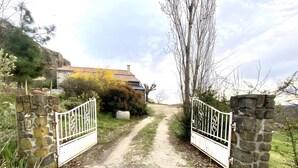 A rural pathway leading to a stone house with a metal gate.