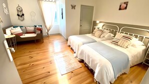 A bedroom with two beds, a bedside table, a chair, a window with curtains, and a door.