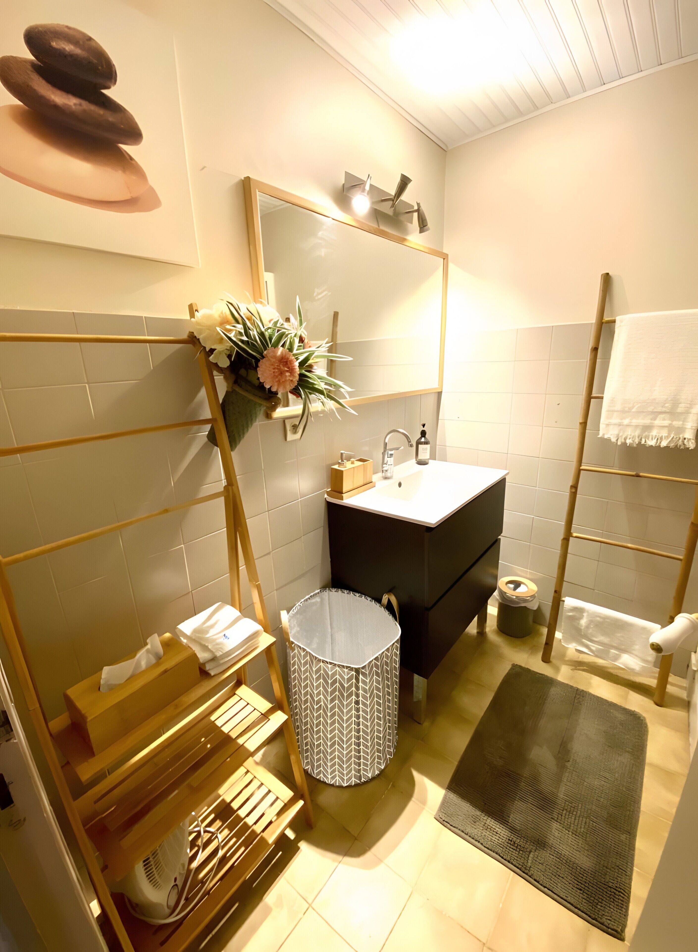 A bathroom with a wooden rack, a sink, a mirror, a trash bin, and a towel rack.
