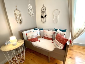 Une pièce chaleureuse avec un canapé, des coussins décoratifs, une petite table avec une lampe et des attrape-rêves accrochés au mur.