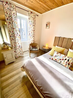Une chambre à coucher avec un lit, une chaise, une table de chevet, une lampe et des rideaux.