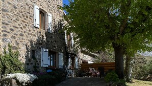 A stone building with a gravel driveway, a large tree, and outdoor seating.