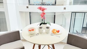 A round white table with two chairs, a potted plant, and a fruit bowl with a plate of fruit.