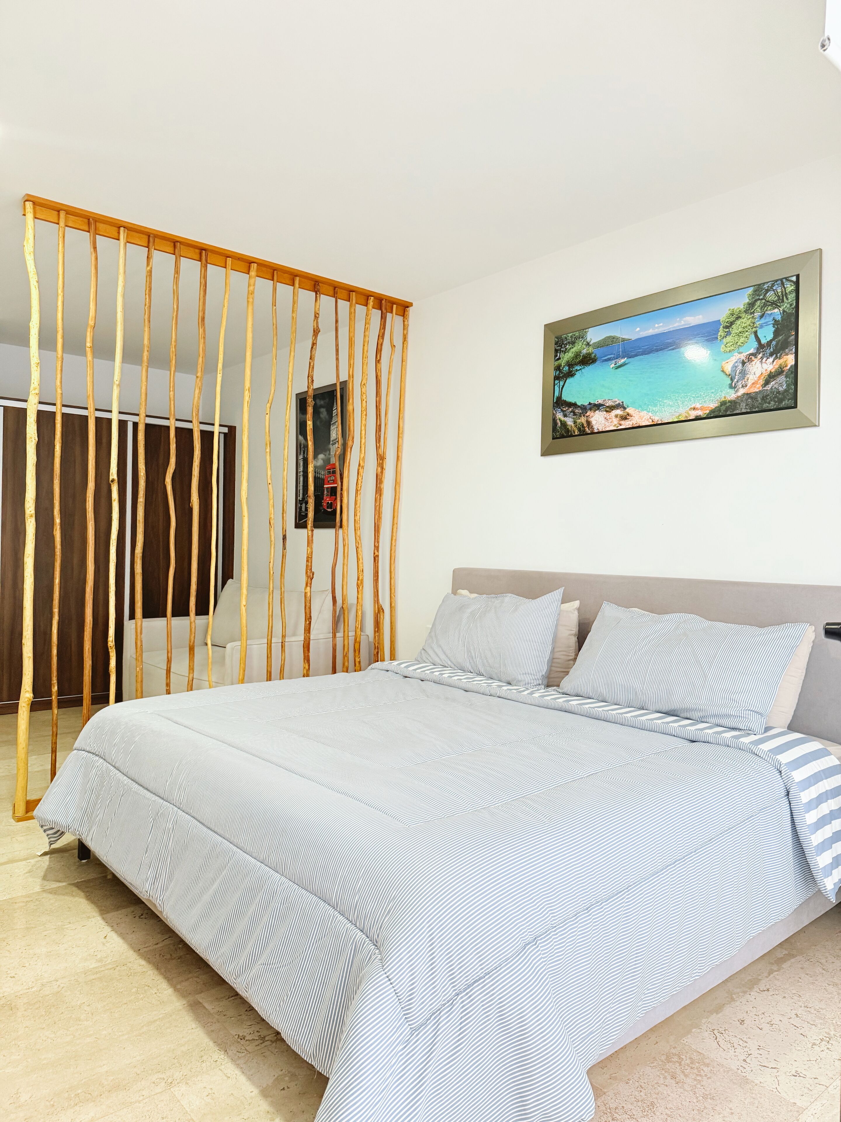 Quarto com cama, divisória de madeira, pintura e vista para a paisagem costeira.