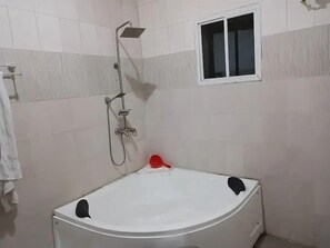 Un baño con una bañera blanca, un cabezal de ducha y un ventanal pequeño.