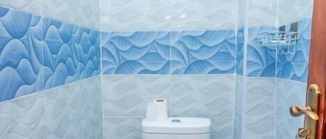 A bathroom with a toilet, a blue patterned wall, and a tiled floor.