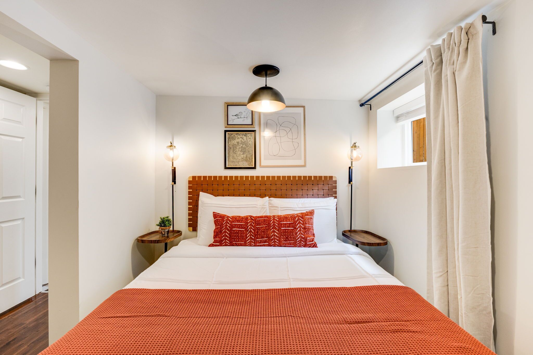 Ein ordentlich eingerichtetes Hotelzimmer mit einem großen Bett, einem Holzkopfbrett, zwei Nachttischen mit Lampen und einem Fenster mit Vorhängen.