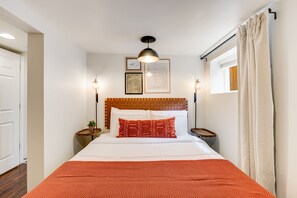 Una camera d'albergo ordinata con un letto grande, una testiera in legno, due comodini con lampade e una finestra con tende.