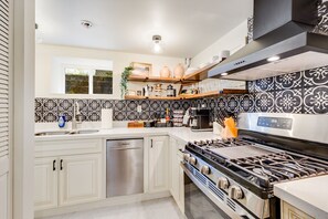 Una cucina moderna con mobili bianchi, una lavastoviglie in acciaio inossidabile, un piano cottura a gas e un angolo caffè.