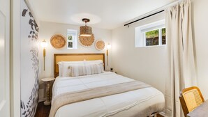 Een slaapkamer met een groot bed, een nachtkastje, een wandlamp en een raam met gordijnen.