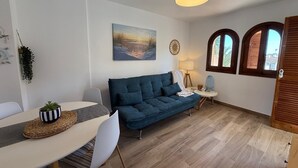 A living room with a blue sofa, a dining table with chairs, a lamp, and a painting on the wall.