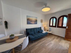 Un salon avec un canapé bleu, une table à manger avec des chaises, une lampe et un tableau au mur.