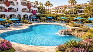 A resort pool area with lounge chairs, umbrellas, and a waterfall feature.