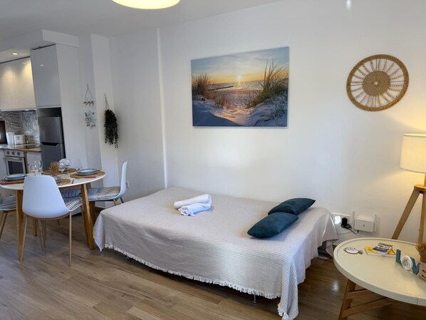 A modern bedroom with a bed, a dining table, and a kitchen area.