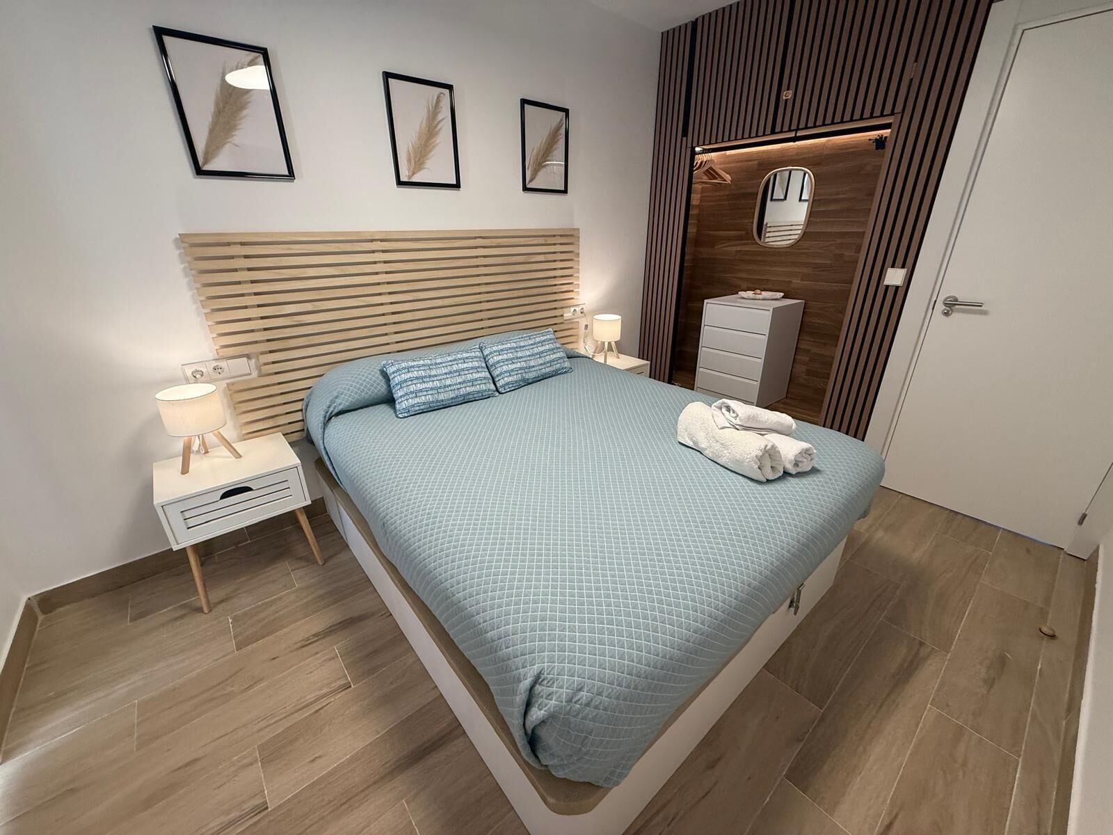 Une chambre moderne avec un grand lit, des tables de chevet, une armoire et des œuvres d’art encadrées accrochées au mur.