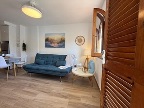 A modern living room with a sofa, a dining table with chairs, a lamp, and a painting on the wall.
