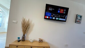 A modern living room with a flat-screen TV mounted on the wall displaying various channels.
