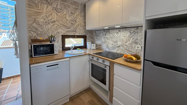 A compact kitchen with white cabinets, a built-in microwave, a sink, and a stove.