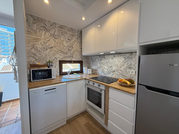 Une cuisine compacte avec des meubles blancs, un four à micro-ondes encastré, un évier et une cuisinière.