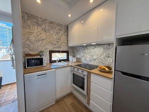 A compact kitchen with white cabinets, a built-in microwave, a sink, and a stove.