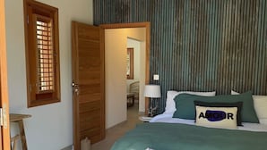 A bedroom with a wooden bed, a bench, a bedside table, a lamp, and a door with a window. - VILLA EDENLY ORIENT BAY (saint martin)